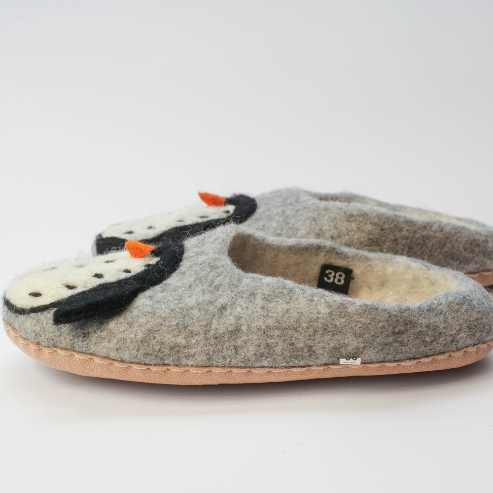 Pinguin Filzpantoffeln Halbschuh Erwachsene, silbergrauer Untergrund, innen naturweiß, Körper des Pinguin Motivs weiß mit schwarzen Punkten, schwarze Flügel, orangener Schnabel. Der Pinguin schaut nach außen zum Kind. Hochgezogene rutschfeste Wildedersohle Marke: MAUSSCHUH by MotherEarth-Munich Ansicht: Von Seite